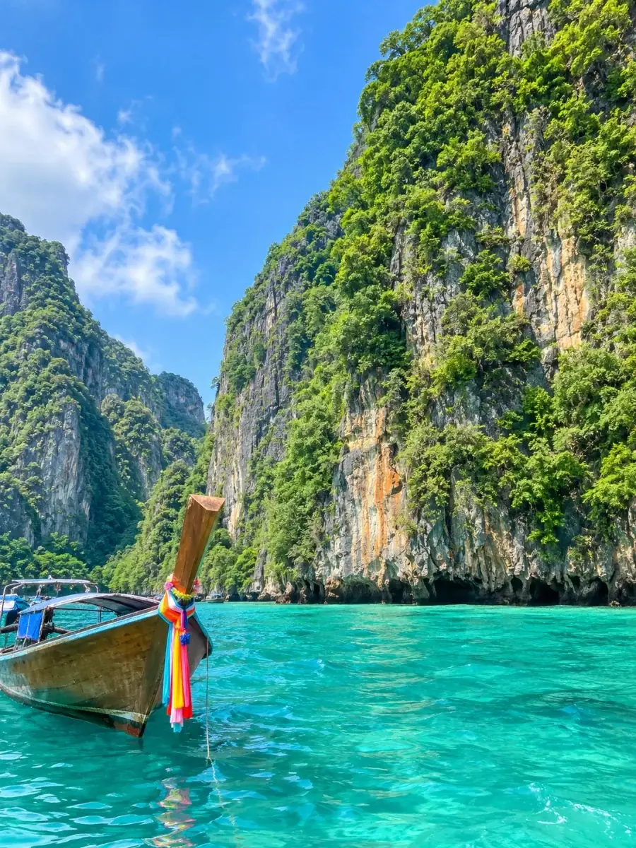 Sheer limestone cliffs of Ko Phi Phi Le draped in jungle above turquoise water, with a ribboned longtail boat in front